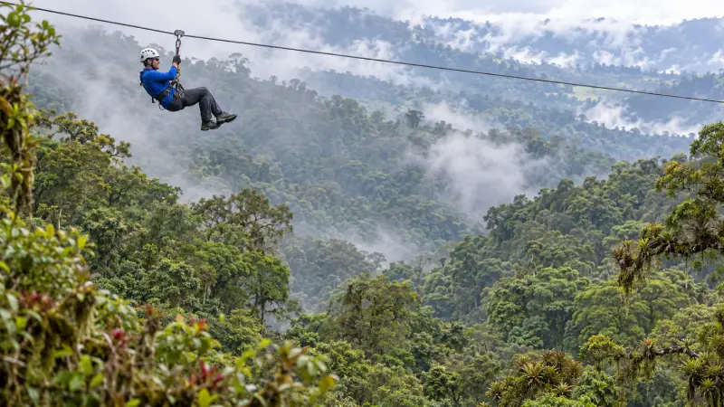 A helmeted visitor ziplining above the cloud-forest canopy at an adventure park near Monteverde.