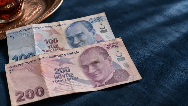Gevouwen blauwe biljetten van 100 lira en paarse biljetten van 200 lira naast een koperen schaal.