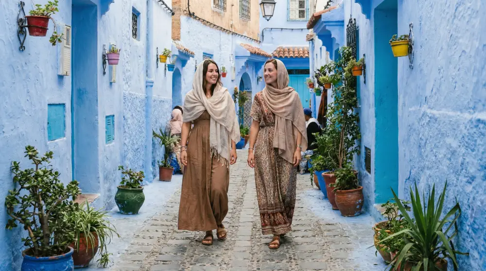 Female tourists dressed modestly in maxi dresses walking safely through a street in Chefchaouen, Morocco.