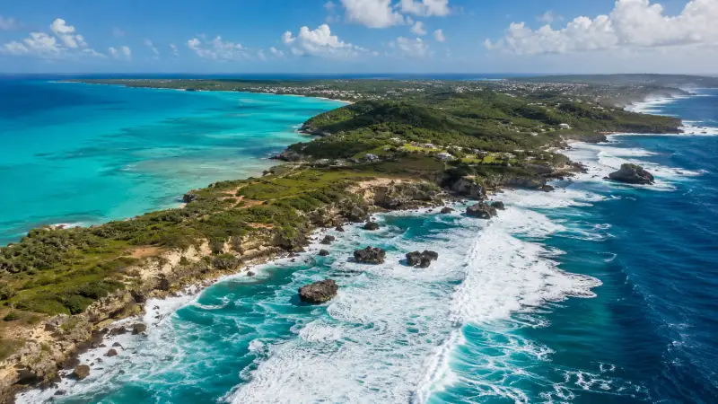 Aerial drone view comparing calm West Coast waters with rugged East Coast Atlantic waves in Barbados.