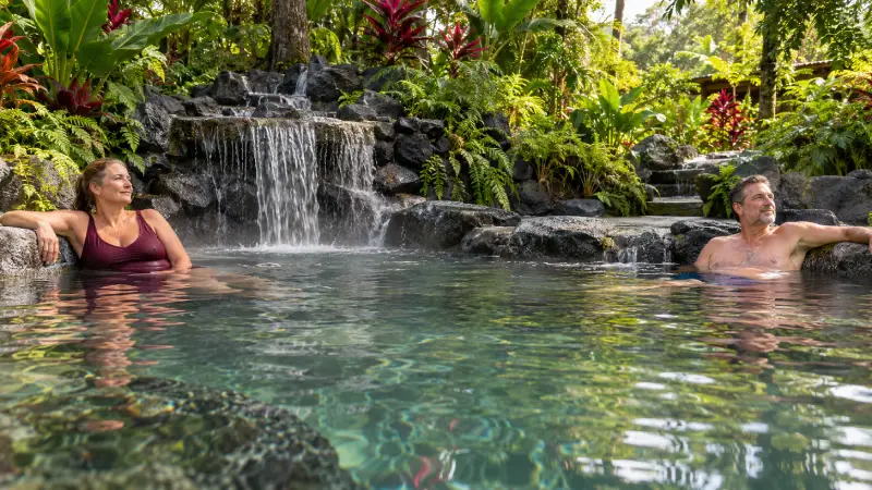 Travellers relaxing in a stone-edged thermal pool surrounded by tropical plants near La Fortuna.