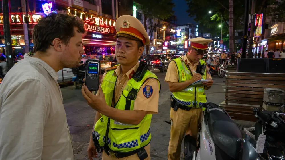 A police officer administering a breathalyzer test to a tourist on a busy Ho Chi Minh City street at dusk.