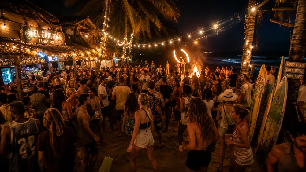 A candid photograph capturing a communal backpacker surf rave on the sand in Tamarindo at night