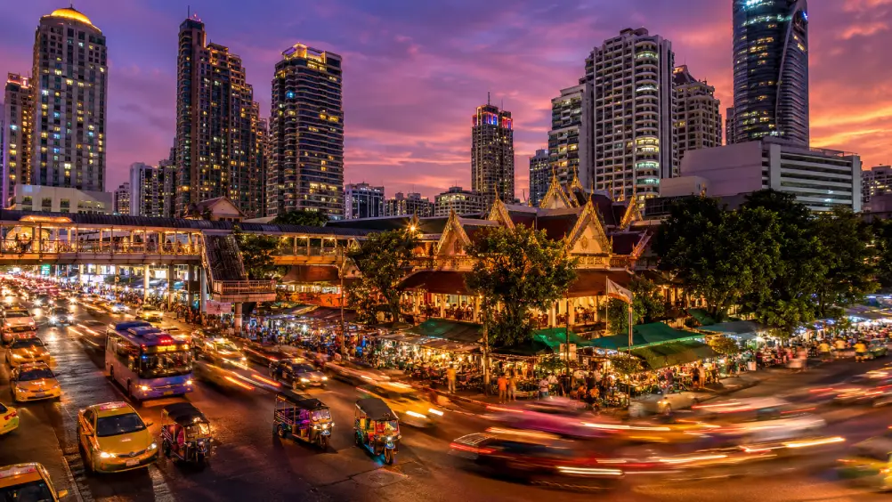 The Bangkok skyline at twilight glowing with neon lights above bustling streets.