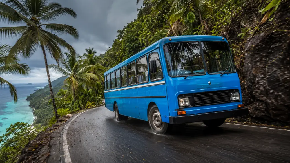 Niebieski autobus publiczny szybko jedzie wzdłuż wąskiej, krętej górskiej drogi otoczonej tropikalną dżunglą na Seszelach.