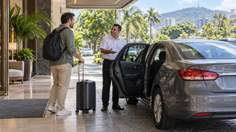 Traveler and driver preparing for a hotel pickup beside a parked sedan in San Salvador.