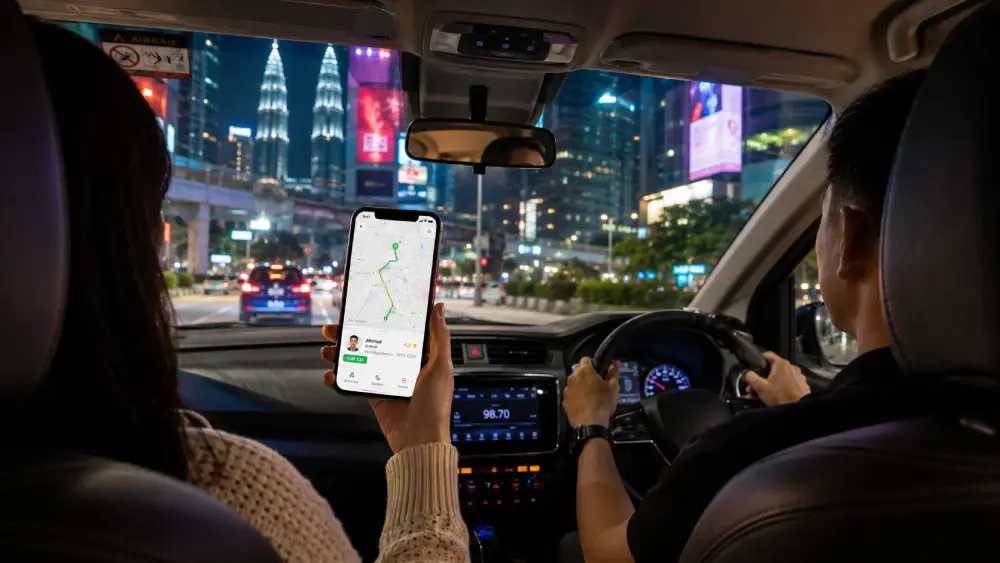 Ein Passagier in einem modernen Fahrzeug, der auf ein Smartphone schaut, das eine verfolgte Mitfahrroute in einer App in Kuala Lumpur anzeigt.
