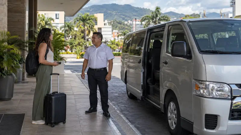 Traveler confirming a pickup with a driver beside a parked passenger van outside a San José hotel.