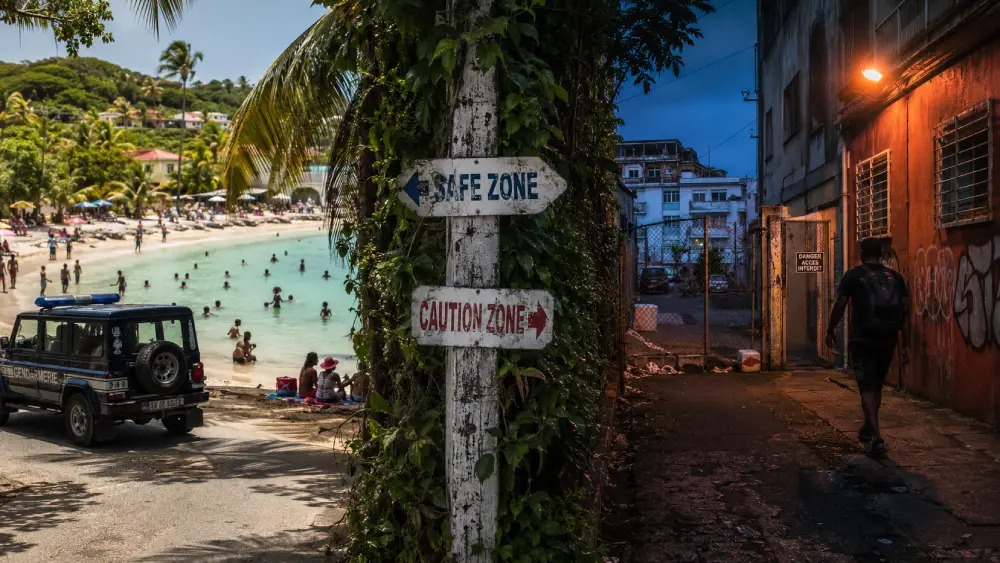 Une photo divisée contrastant une plage sûre baignée de soleil à Sainte-Anne avec une ruelle urbaine ombragée et crasseuse à Pointe-à-Pitre au crépuscule.