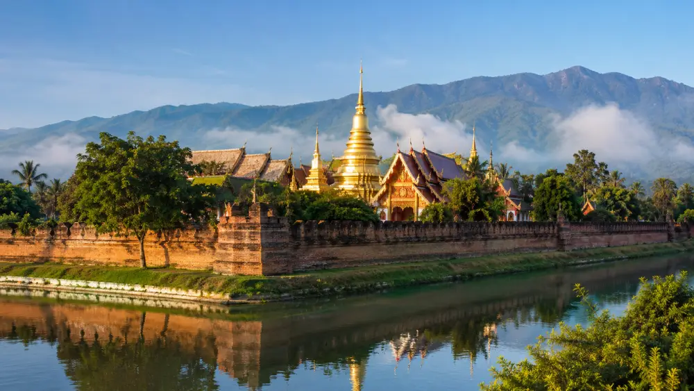 Golden temples inside the ancient moat walls of Chiang Mai with mountains in the background.