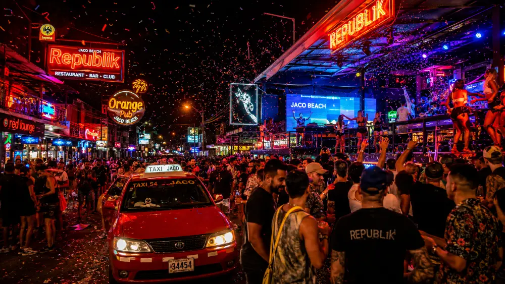 A vibrant photograph showcasing the garish neon chaos of Jac&oacute; Beach's Pastor Diaz Avenue at night