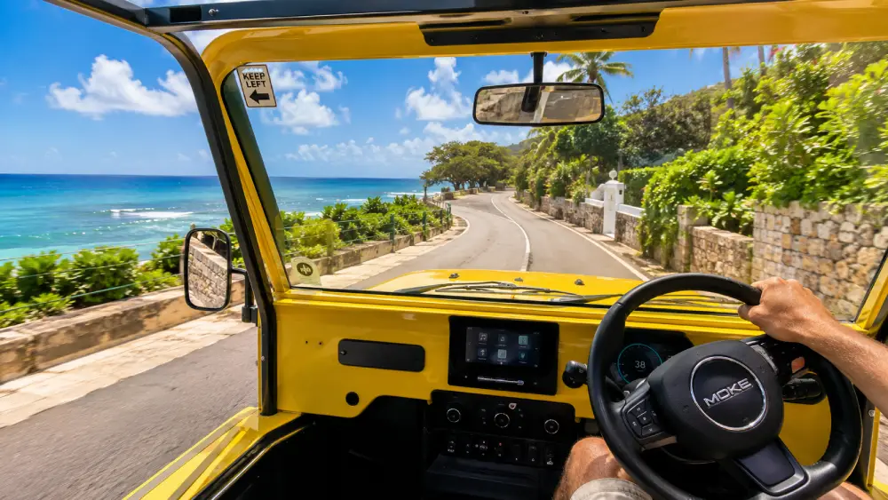 Driving a rental car on the left side of a Barbados coastal road with a right-hand drive steering wheel.