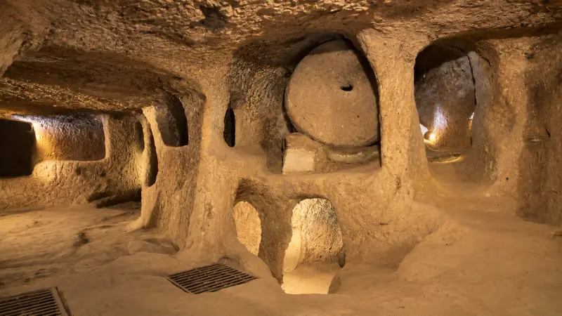 Rock-cut chamber, narrow openings and a circular stone door inside Kaymaklı Underground City.