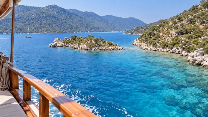 Turquoise water and rocky, scrub-covered shores in the Kekova region, viewed from an excursion boat.