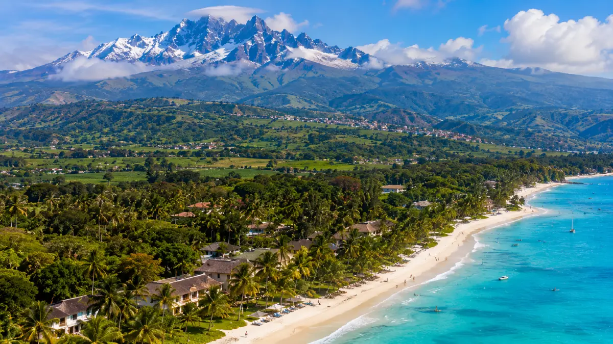 Un paesaggio che evidenzia la diversità geografica del Kenya, mostrando la cima innevata e nebbiosa del Monte Kenya sullo sfondo, e palme tropicali e la spiaggia turchese di Diani in primo piano.