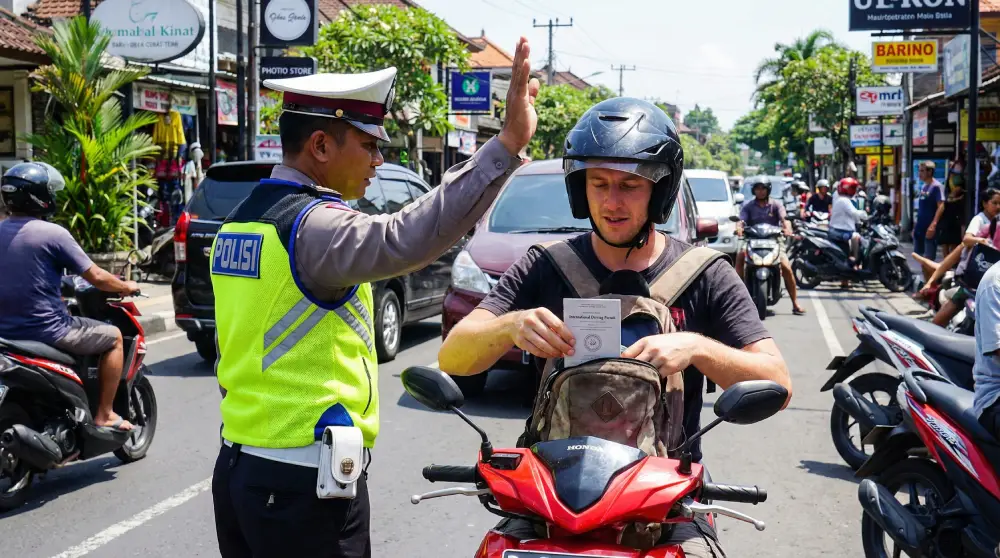 Foreign tourist on a scooter being stopped by an Indonesian traffic police officer at a Bali checkpoint for an International Driving Permit check.