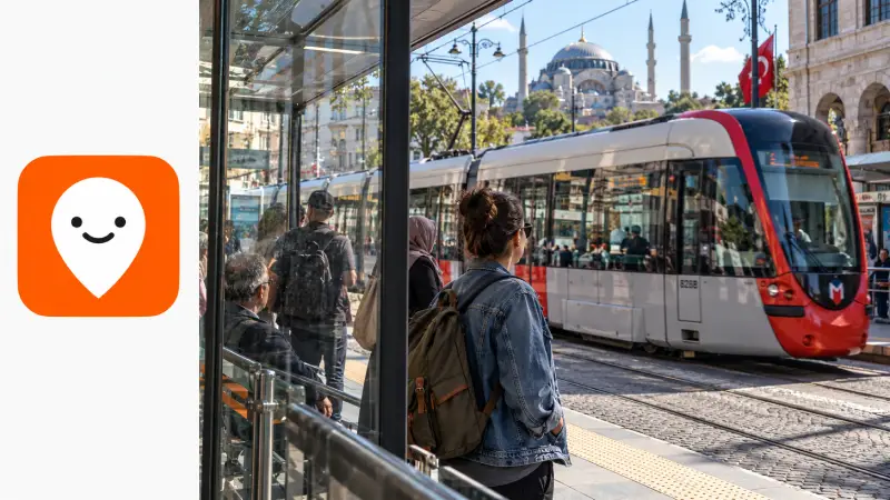 Tramhalte in Istanbul gezien door het reflecterende glas van een abri, met het officiële oranje Moovit-pictogram in een redactionele marge.