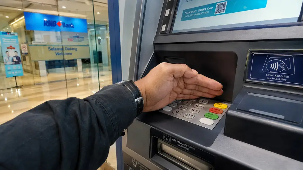 Eine Nahaufnahme eines Touristen, der sicher einen sicheren Geldautomaten in einer hell erleuchteten, modernen Bankfiliale in Malaysia benutzt.