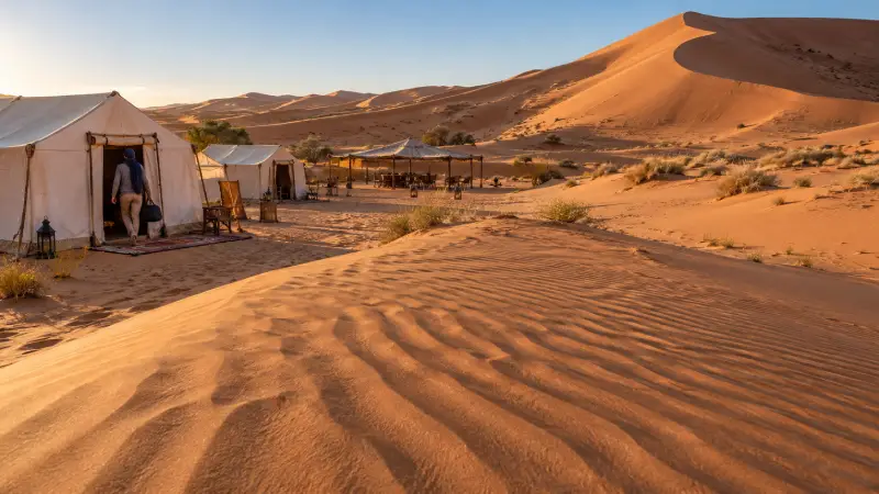 Illustrative Merzouga desert camp with canvas tents and a dining shelter beside the Erg Chebbi dunes.