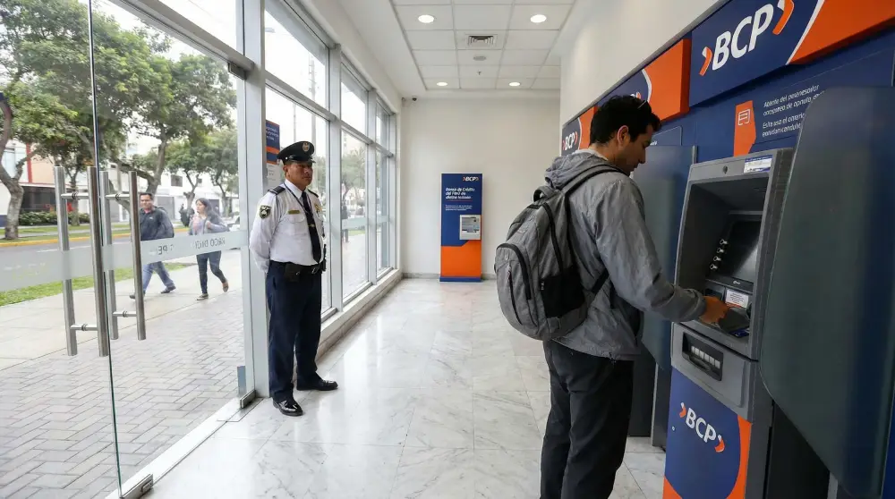 Um turista usando um caixa eletrônico com segurança dentro de uma agência bancária segura em Lima para evitar fraudes de skimming.